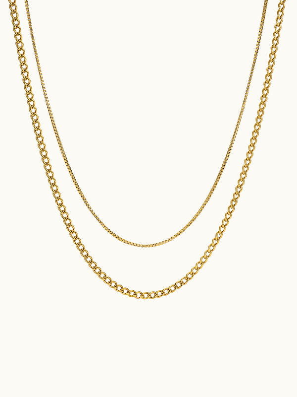 A double layered necklace with one chain featuring a box link design and the other with a curb link design, both in gold color.